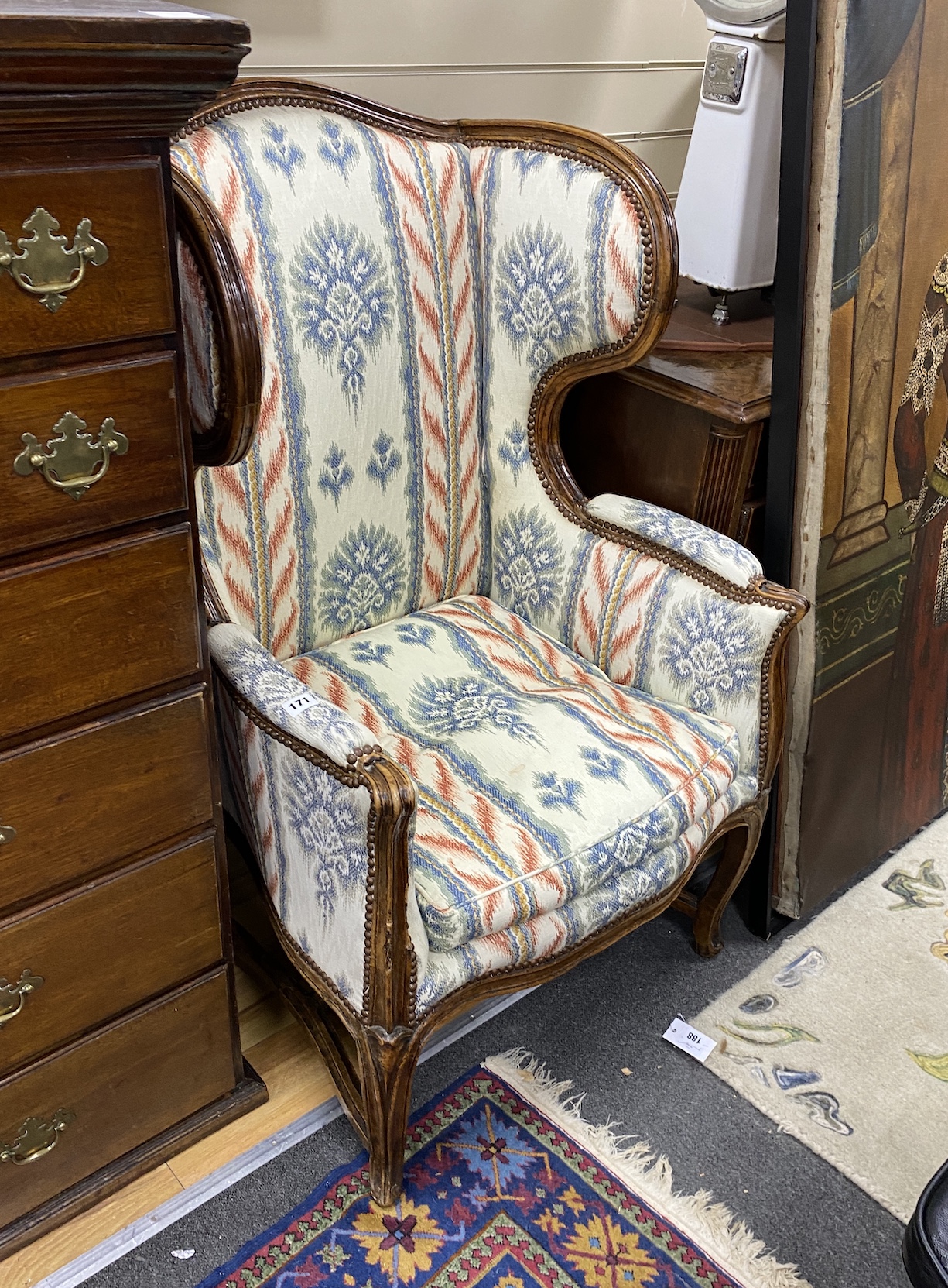 A Louis XV Provincial walnut wing armchair, with moulded frame, arched stuffed back loose cushion seat and cabriole legs joined by stretchers, width 63cm, depth 70cm, height 115cm